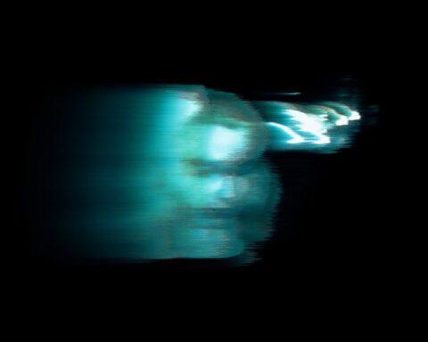 Blurry image of a person lit by blue-green lighting.