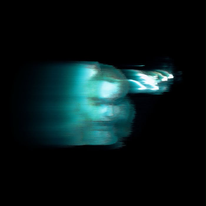 Blurry image of a person lit by blue-green lighting.